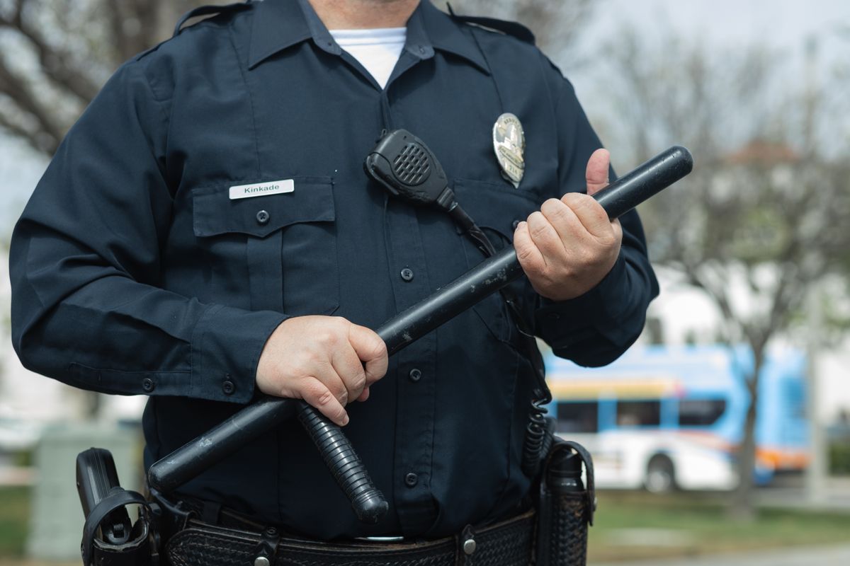 Uniformed police officer holding a baton, a less-lethal use of force option, on his duty belt