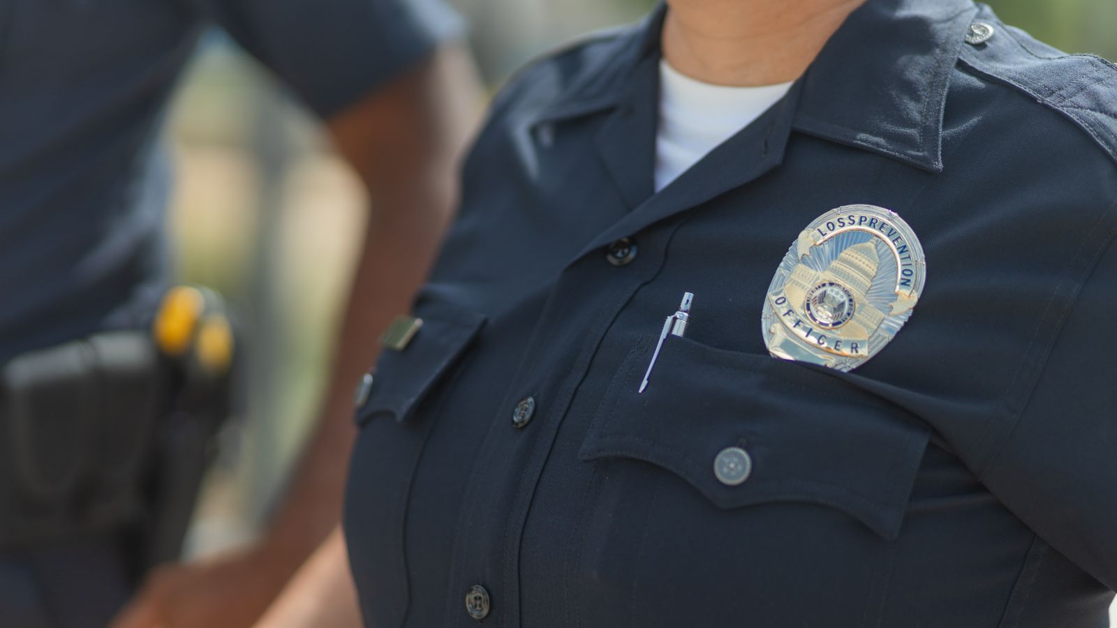 Close-up of police officers in uniform, displaying badge and radio outdoors.