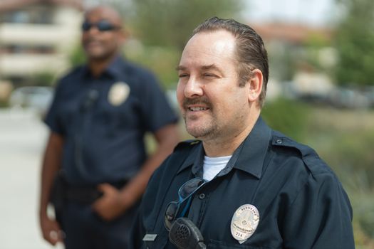 Two police officers smiling outdoors in uniform, representing community service.