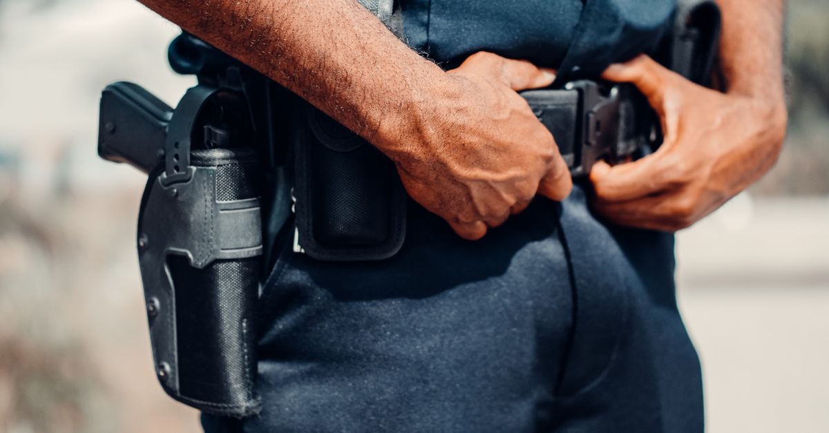 A police officer adjusts their utility belt outdoors, showcasing law enforcement gear and uniform.