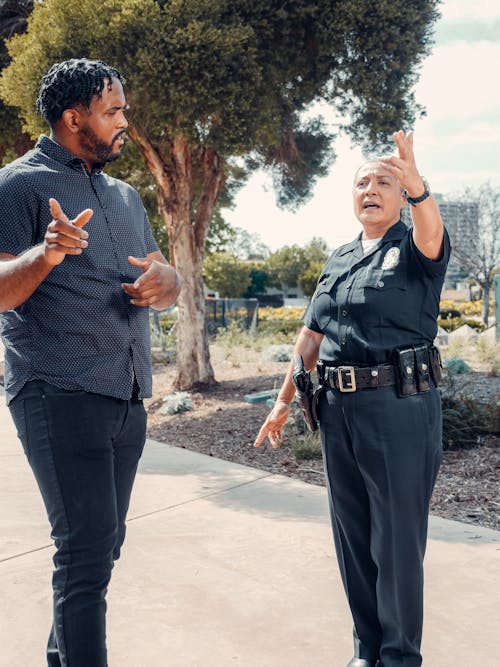 Man in Black and White Button Up Shirt Talking to Woman in Police Uniform