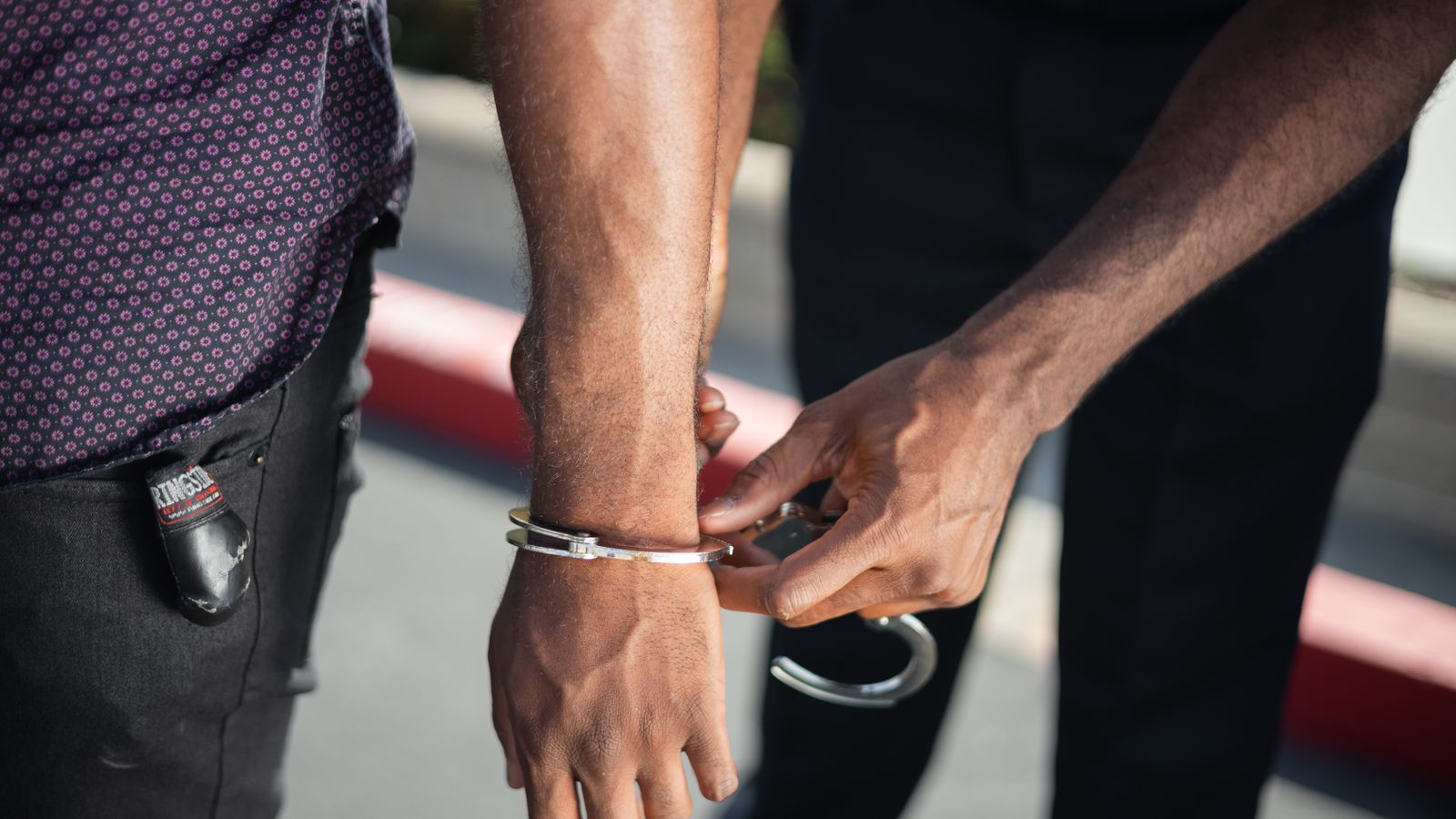 Close-up of a police officer handcuffing a suspect outdoors, enforcing law.