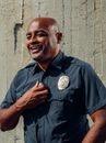 A cheerful police officer in uniform smiling while holding a radio outdoors.