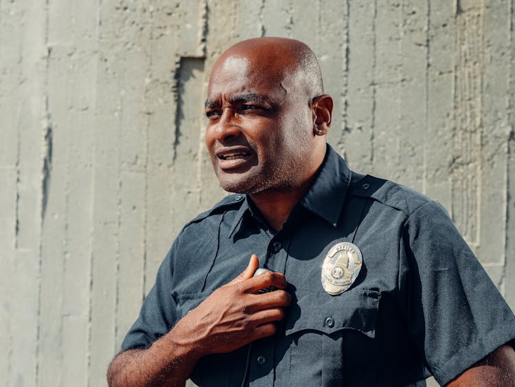 Man In Black Police Uniform Standing Beside Gray Concrete Wall