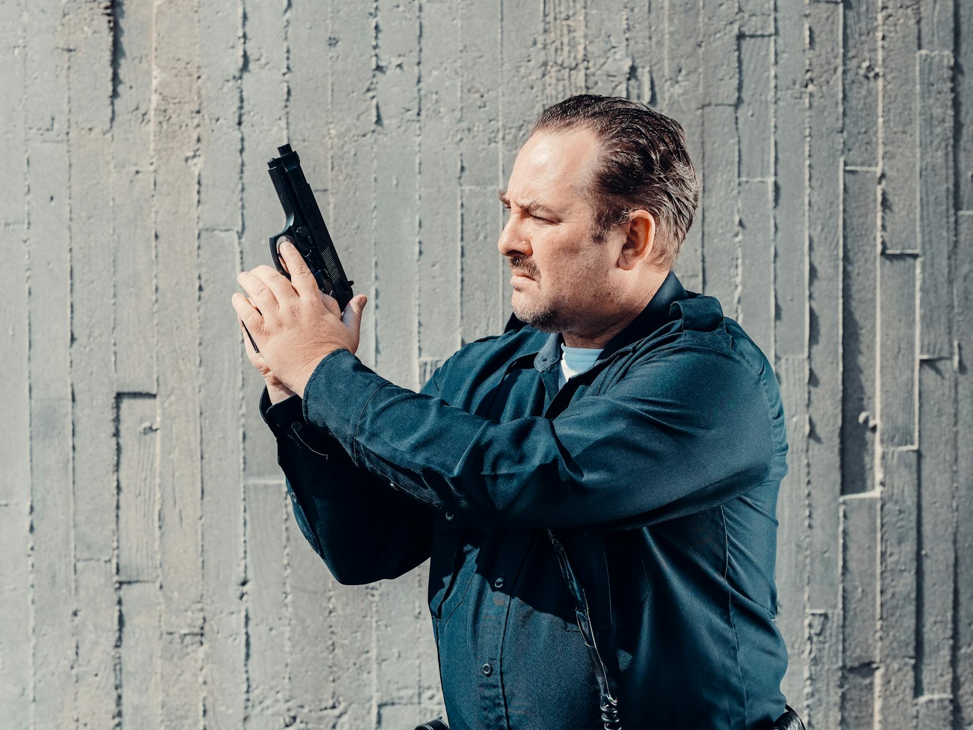 A Police Officer Holding a Gun while Standing Near Gray Wall