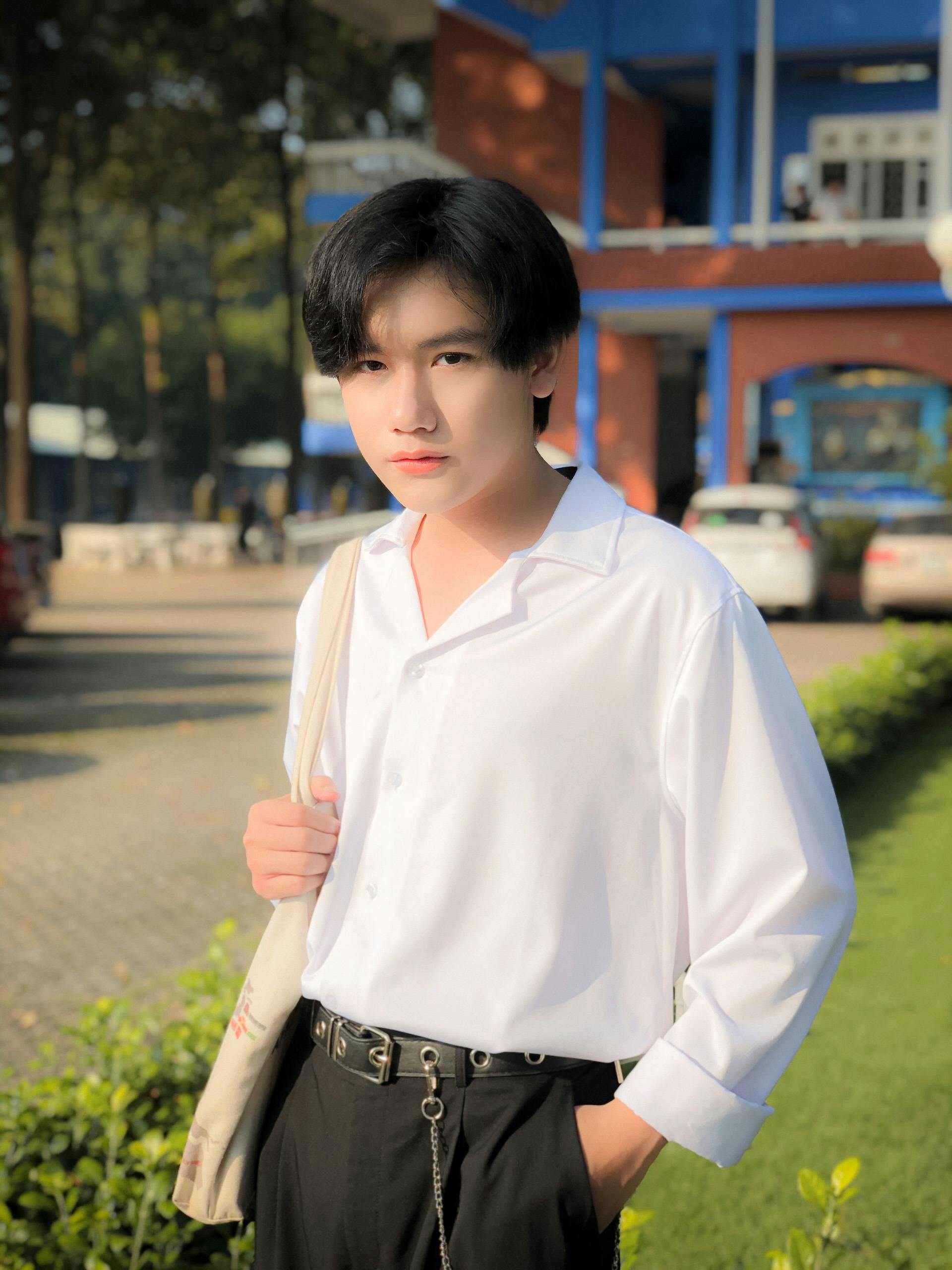 Young man in white shirt standing outdoors, embracing casual fashion with natural light.
