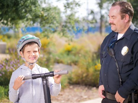 A police officer smiling at a boy on an electric scooter in a park setting, promoting community safety.
