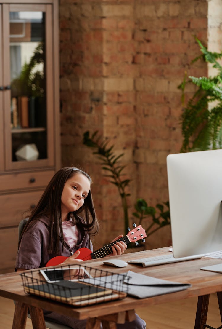 A Girl Learning To Play Ukulele Through Online Lesson