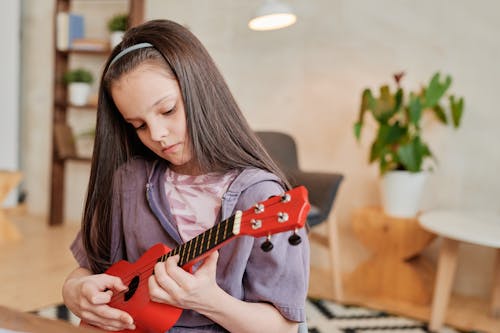 Photograph of a Girl Playing a Red Ukulele