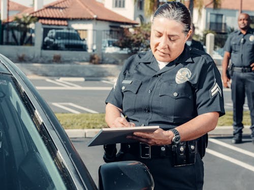 A Police Officer Standing Beside a Car while Holding a Clipboard