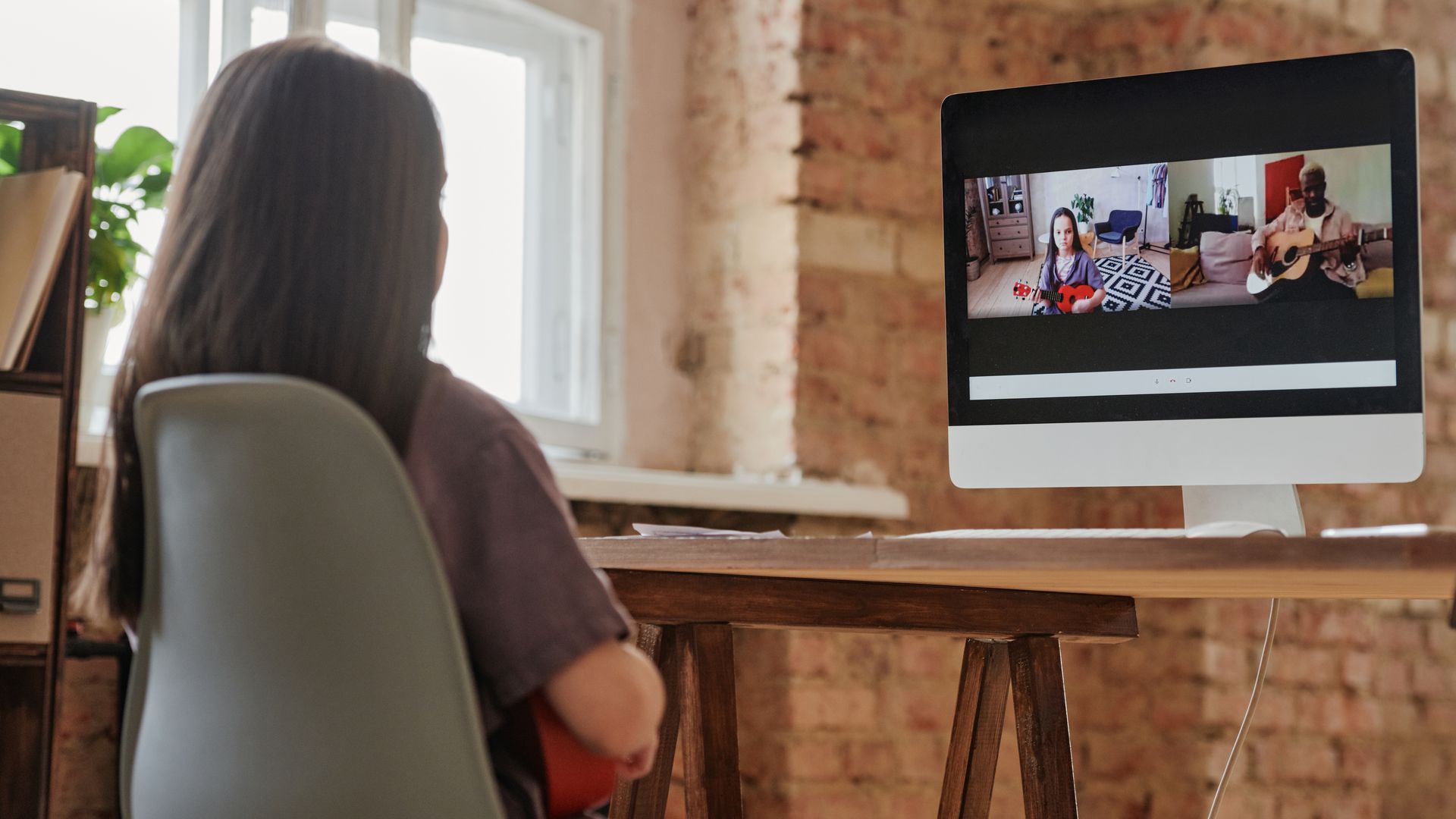 Young girl taking an online music lesson playing ukulele at home.
