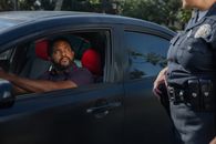 Man in Red Shirt and Gray Jacket Leaning on Black Car Door