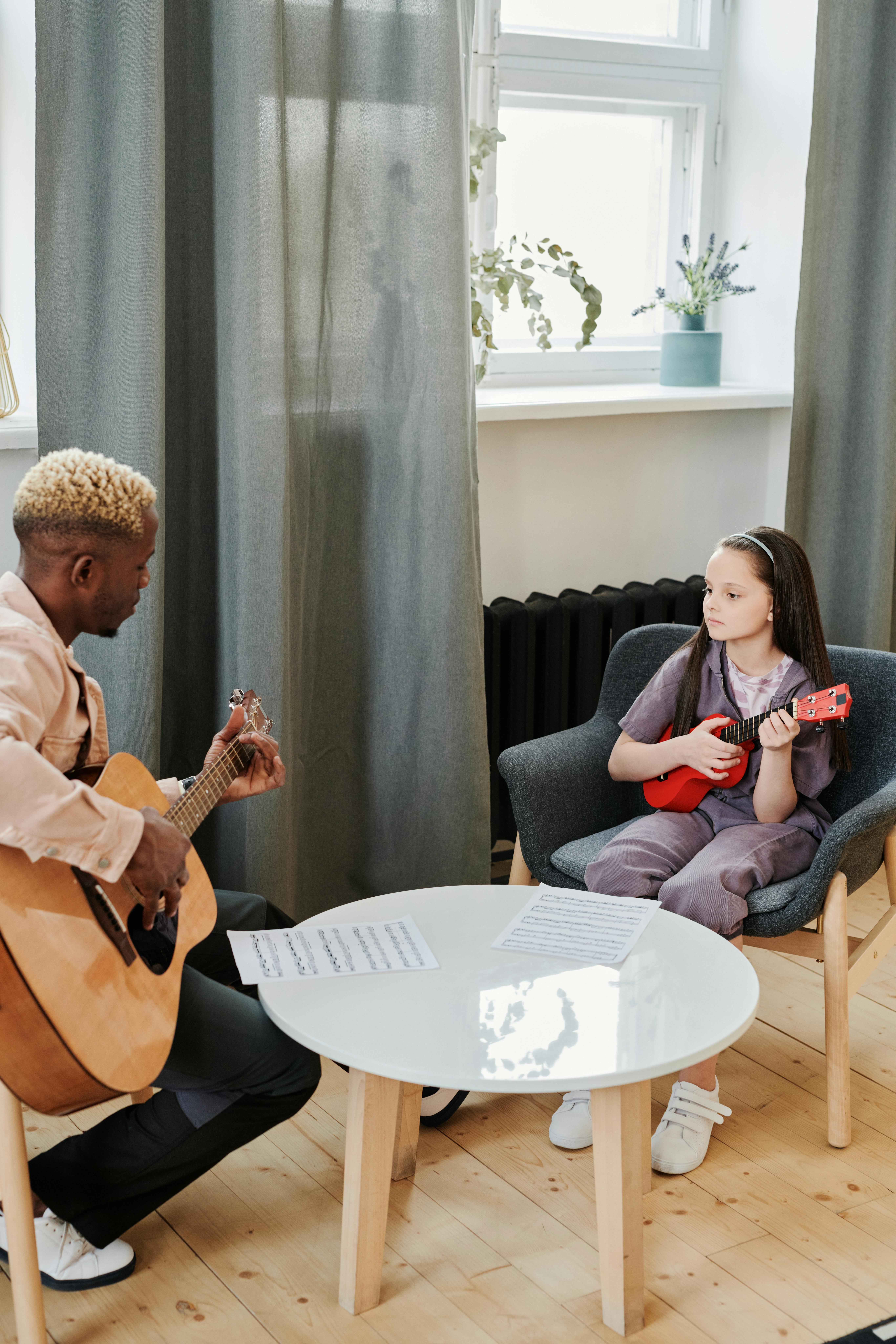 Young student learning ukulele from an instructor playing guitar in a cozy room.