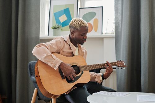 Free Young adult playing acoustic guitar in a cozy room, enjoying a musical moment. Stock Photo