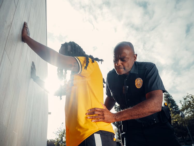 A Police Officer Frisking The Person In Yellow T-Shirt 