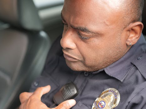 Close-up of a police officer in uniform using a radio in a patrol car, focused on communication.