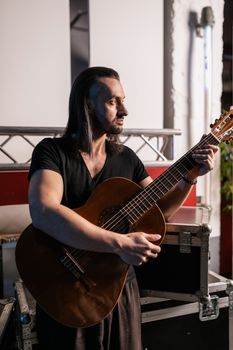 A bearded man with long hair plays guitar indoors, creating a musical ambiance.