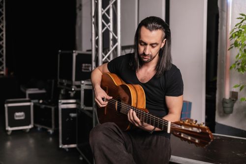 Free Musician with long hair and a black shirt playing an acoustic guitar in a studio setting. Stock Photo