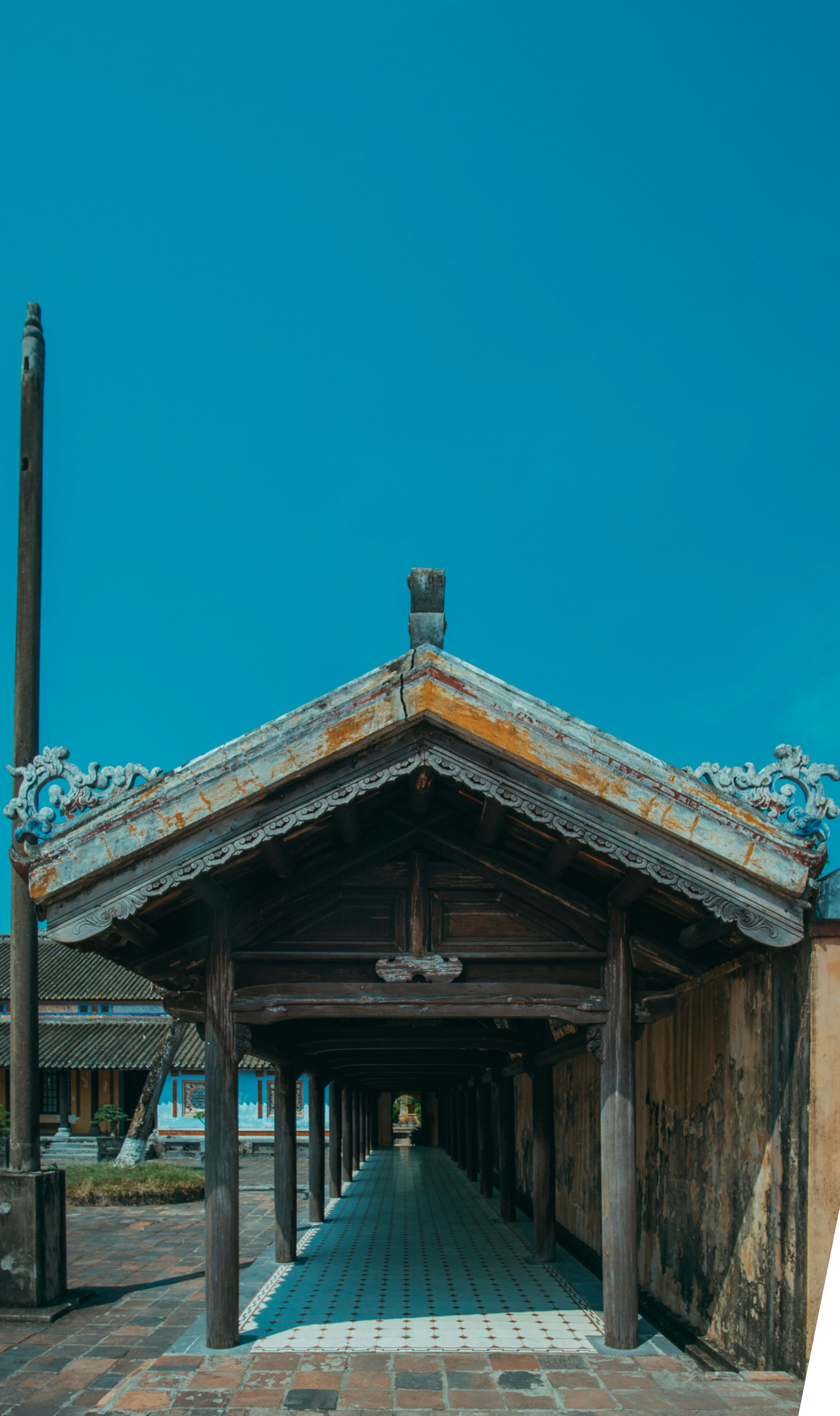 Explore the intricate wooden architecture of a traditional temple corridor under a clear blue sky.