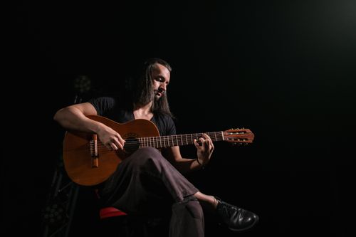Free A musician with long hair sitting and playing a guitar in a dark room. Stock Photo