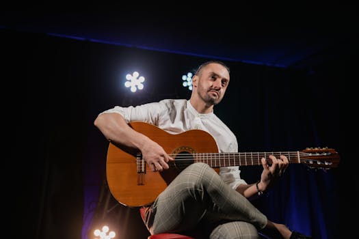 A musician playing an acoustic guitar on stage under dramatic lighting.