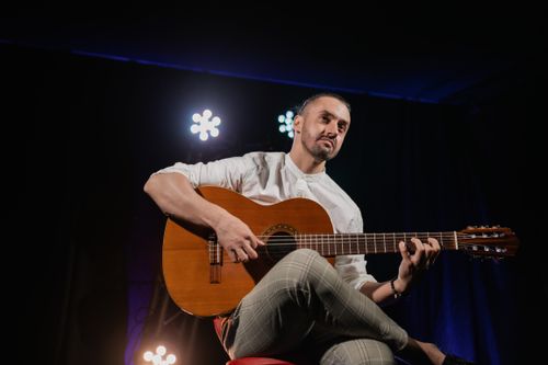 Free A musician playing an acoustic guitar on stage under dramatic lighting. Stock Photo
