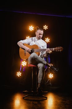 Male guitarist playing acoustic guitar on stage under warm spotlight.