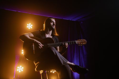 Free Musician playing guitar under dramatic stage lighting in a club setting. Stock Photo