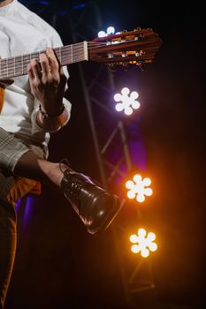 Musician playing guitar on stage with vibrant stage lights and leather shoes, capturing live performance energy.