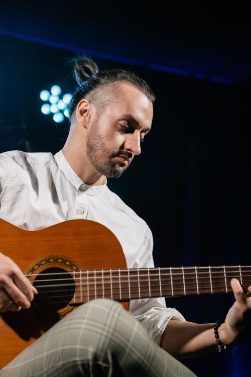 Free A bearded man in a white shirt skillfully playing an acoustic guitar on stage. Stock Photo