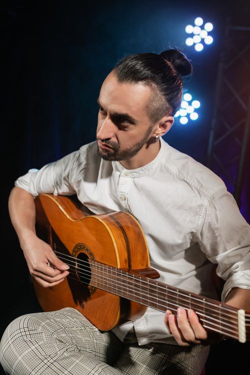 Free Portrait of a musician playing acoustic guitar under stage lights. Stock Photo