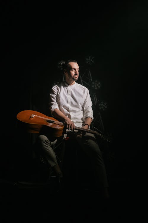 Man in White Long Sleeves Holding a Guitar While Sitting