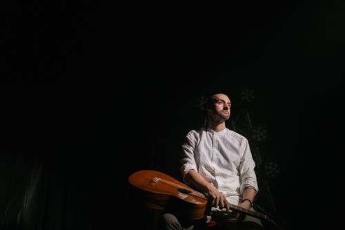 Free A man holding a guitar sits pensively in dramatic lighting against a dark background. Stock Photo