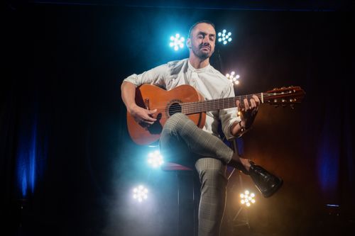 Free A man with closed eyes plays guitar on stage, with dramatic lighting enhancing the mood. Stock Photo