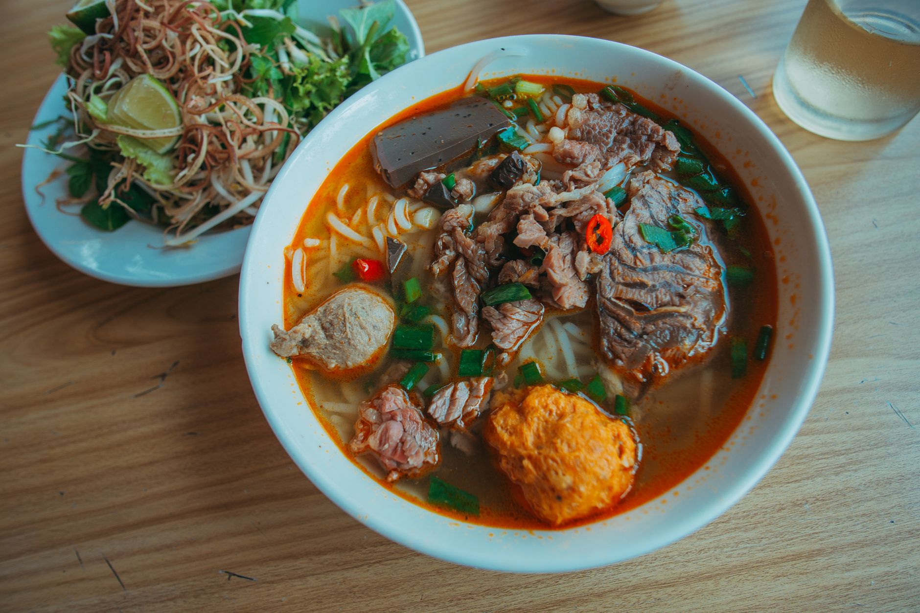 A mouth-watering bowl of Vietnamese beef noodle soup with fresh herbs and vegetables on a wooden table.