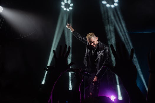 Energetic DJ in a leather jacket performing live under vibrant stage lights with an enthusiastic crowd.