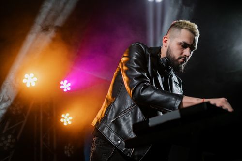 Free A male DJ wearing a leather jacket performs under colorful stage lights, creating an energetic ambiance. Stock Photo