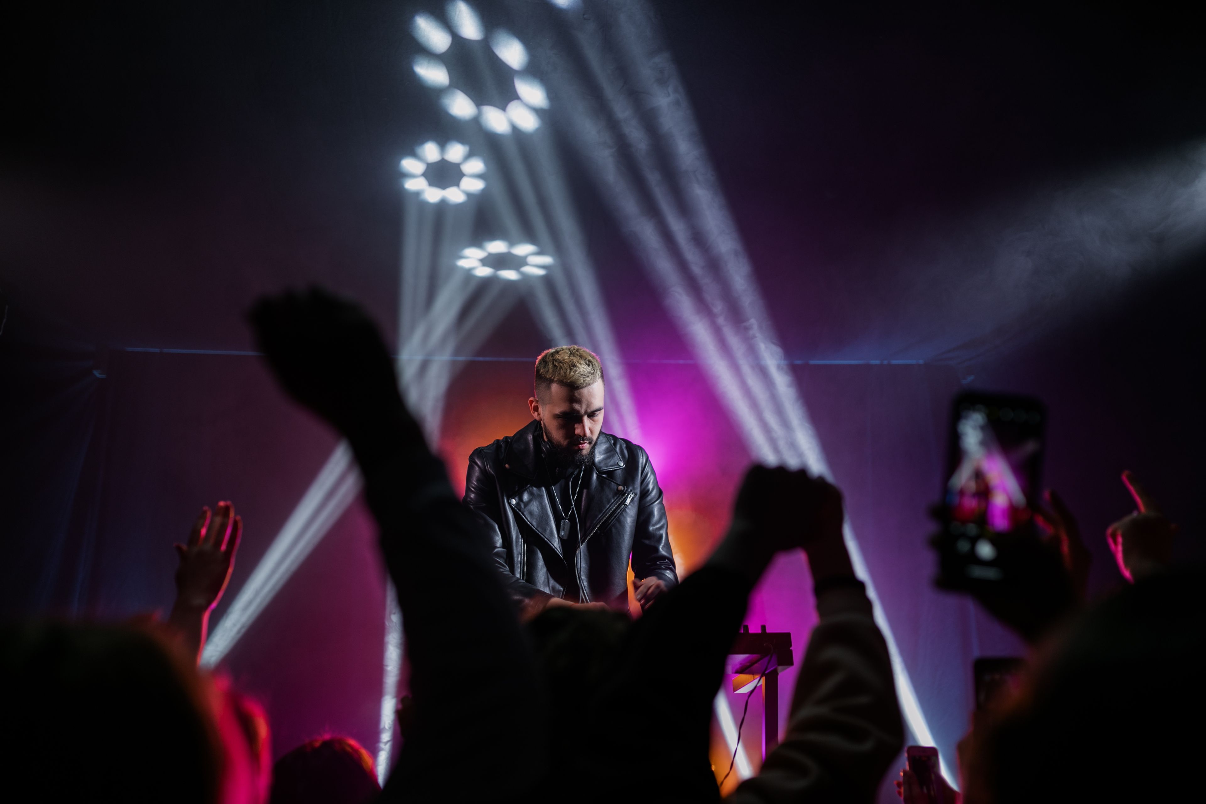A DJ playing to a crowd under sweeping coloured beams