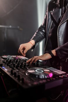 A DJ skillfully mixes music on a DJ mixer while wearing a leather jacket.