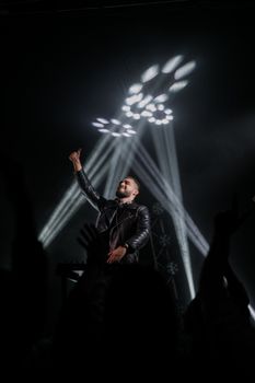 Musician on stage in leather jacket with vibrant light effects at concert.