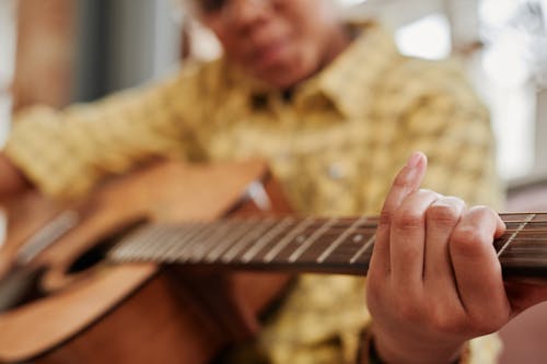 Close-Up Photo of a Person in a Yellow Shirt Playing the Guitar