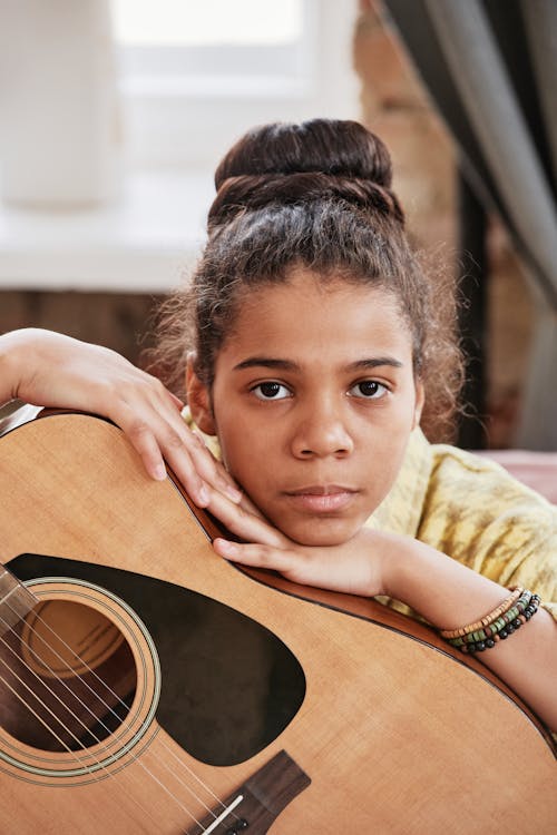 Close-Up Photo of a Girl Leaning on a Brown Acoustic Guitar