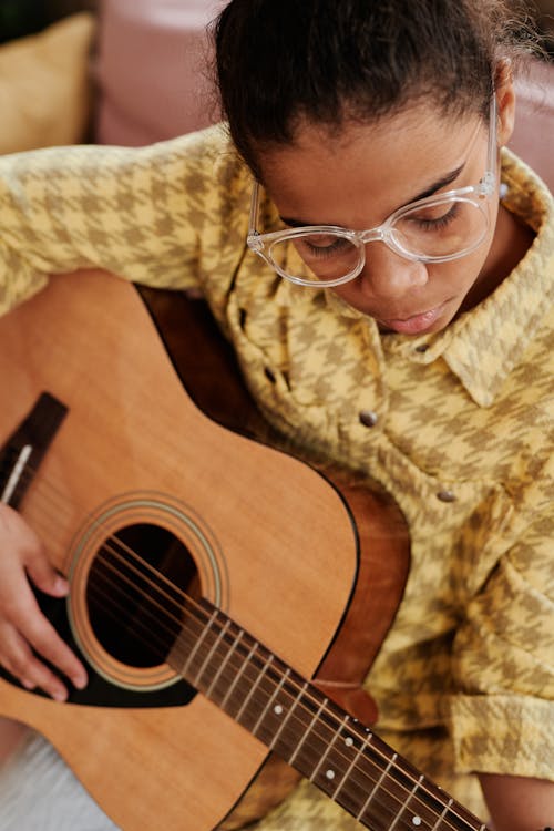 High-Angle Shot of a Girl in a Yellow Shirt Playing an Acoustic Guitar