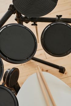 Aerial perspective of an electronic drum set and two wooden drumsticks on a stool.