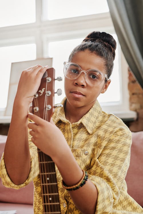 Close-Up Photo of a Girl in a Yellow Shirt Holding a Guitar