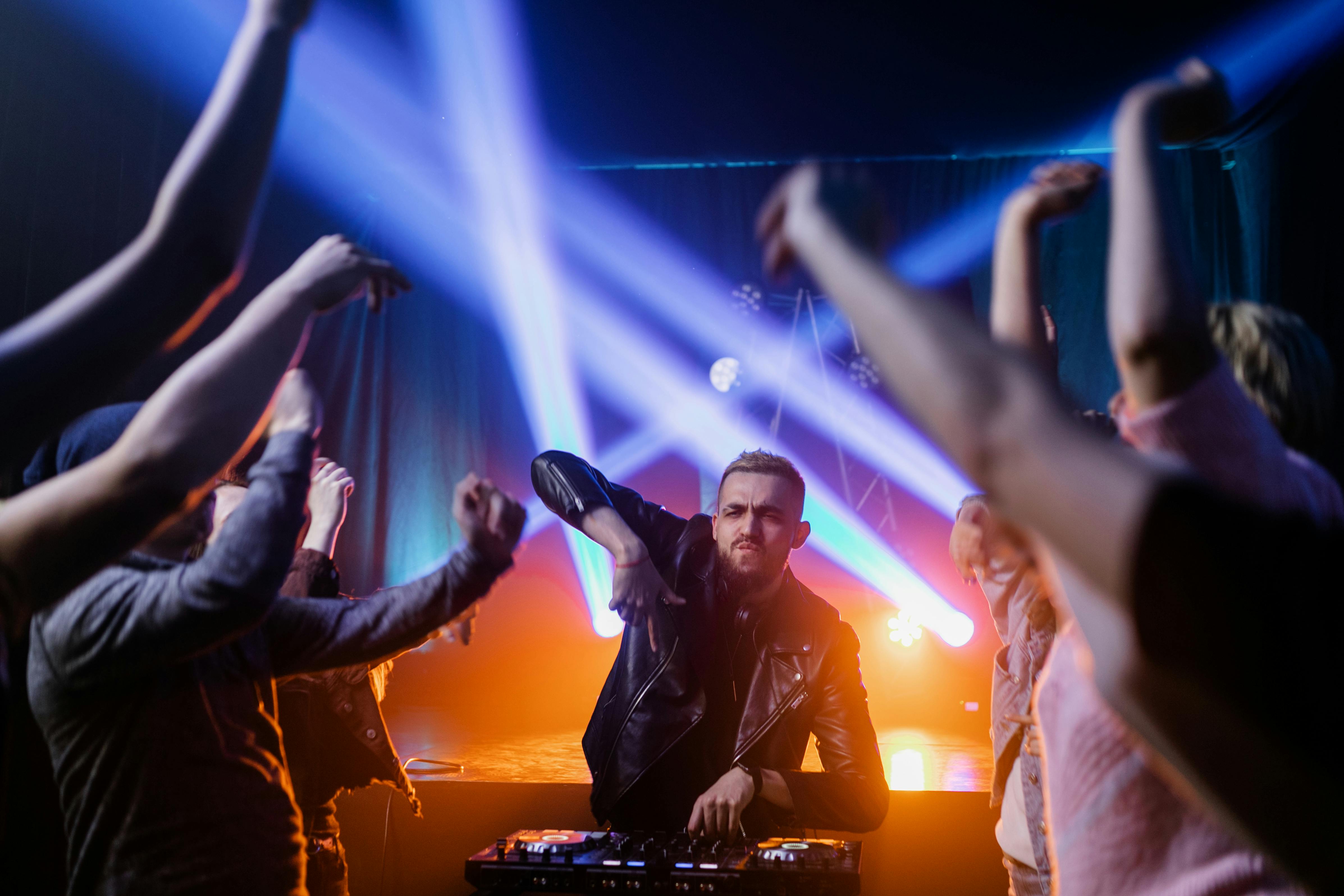 crowd dancing beside a man in black jacket playing the dj mixer