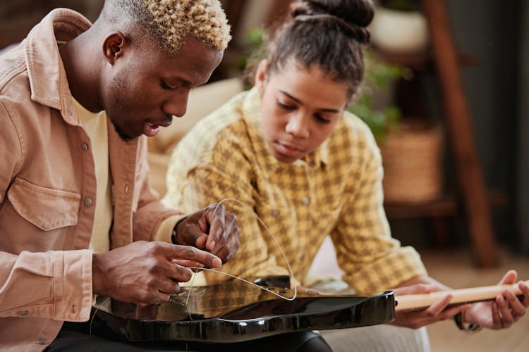 A Man Fixing Guitar String Beside A Girl