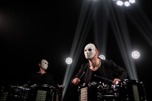 Two masked drummers engage in a dynamic percussion performance under dramatic stage lighting.