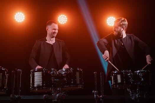 Energetic percussion performance by two drummers under vibrant stage lighting.