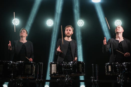 Three drummers perform with striking lighting effects on stage.